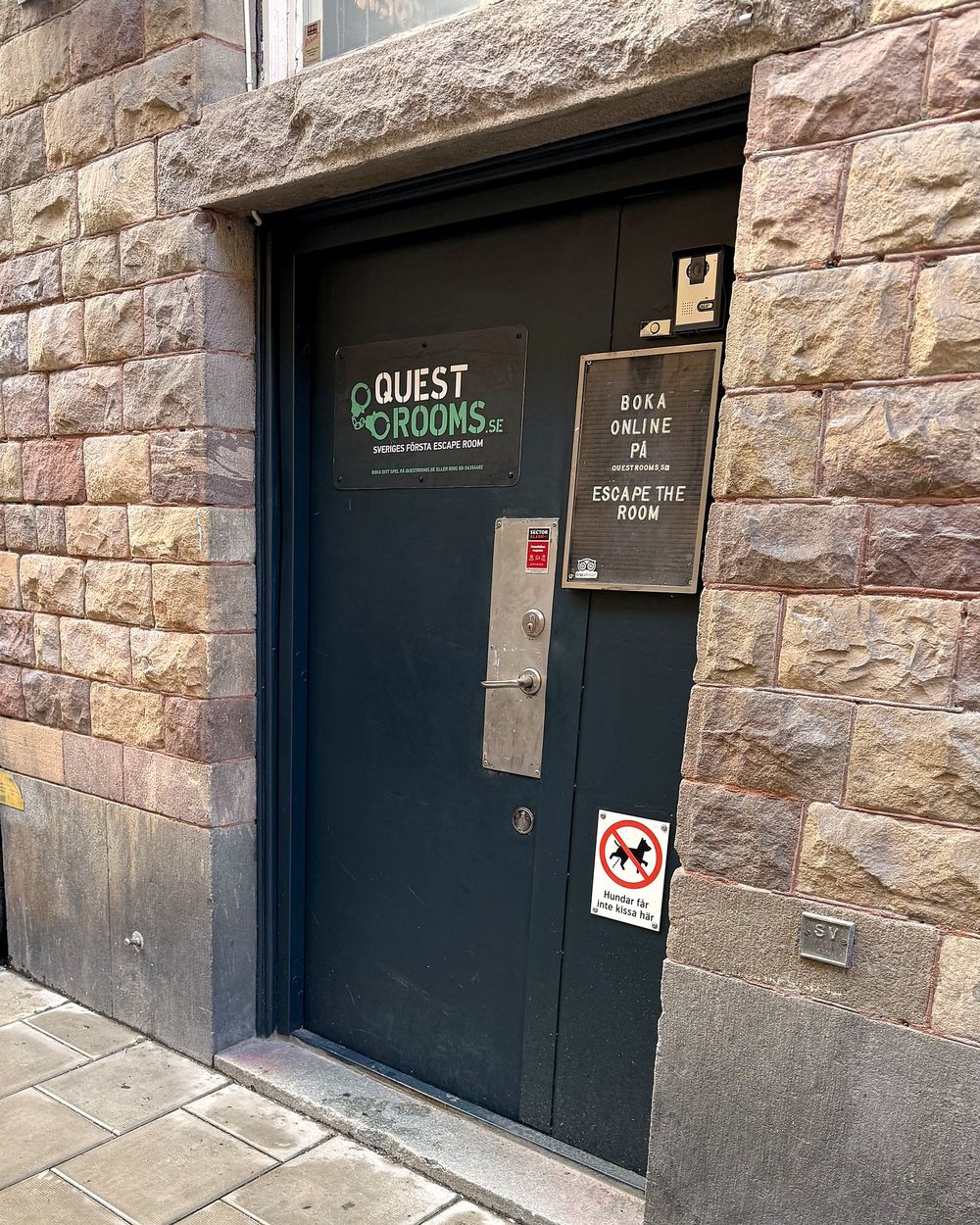 The entrance seen from the pavement, a black door in the stone facade